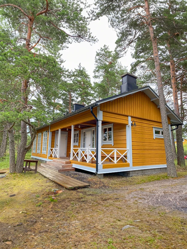 This image showcases a charming yellow wooden cabin with a porch, surrounded by lush trees, offering a serene and inviting atmosphere.