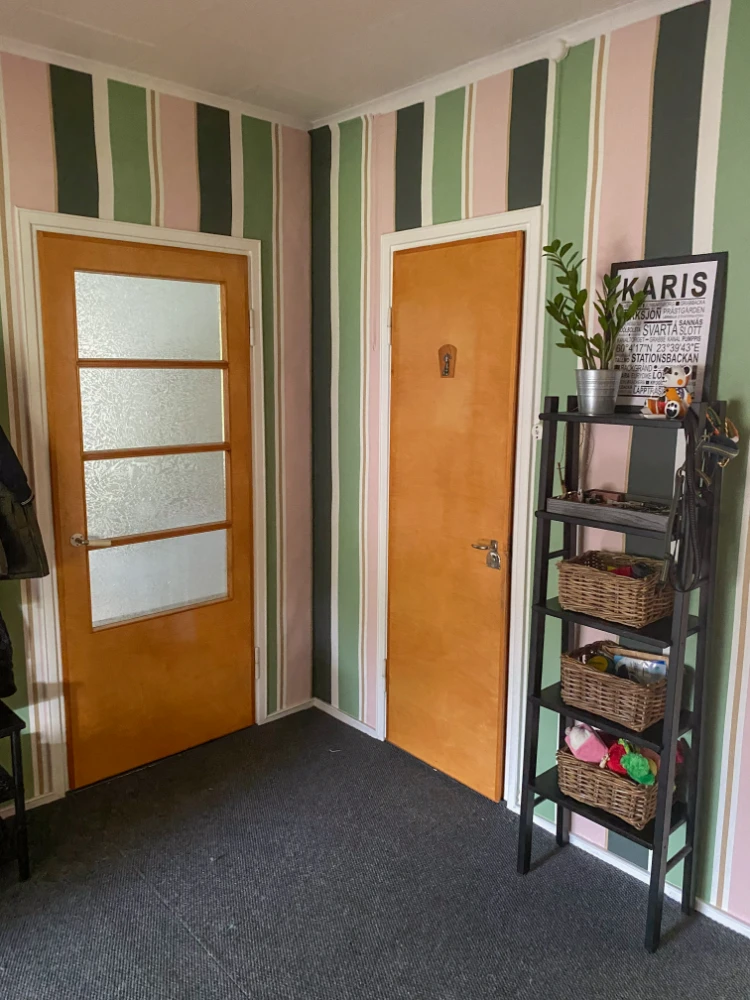The image shows an entryway or hallway with a striped wallpaper pattern in shades of pink, green, and black.