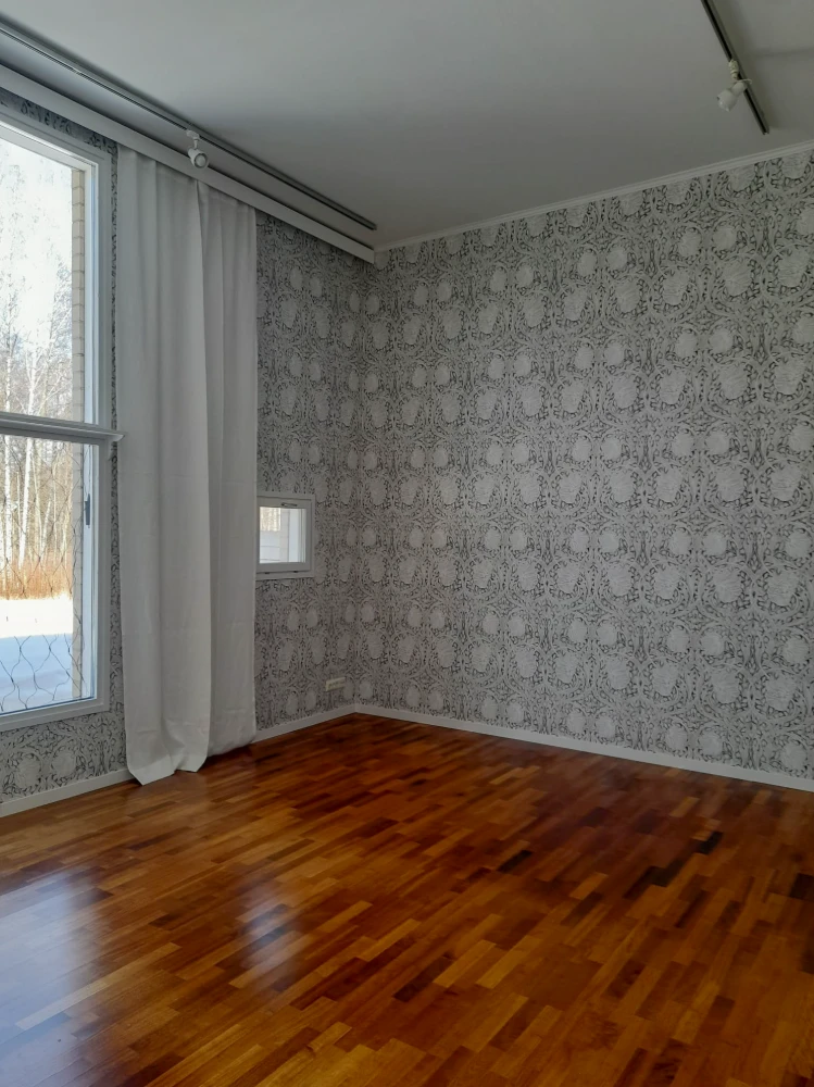 Empty room with patterned wallpaper and wooden flooring. The room has a large window that provides natural lighting.