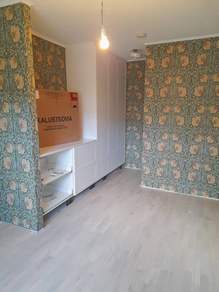 The image shows a room with floral patterned wallpaper covering the walls. There is a large cardboard box .