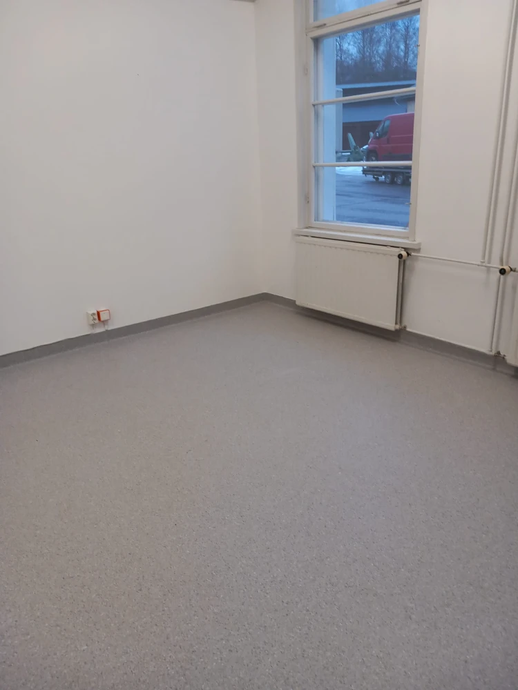 Empty room with a window overlooking a snowy outdoor scene. The room has a grey concrete floor and white walls.