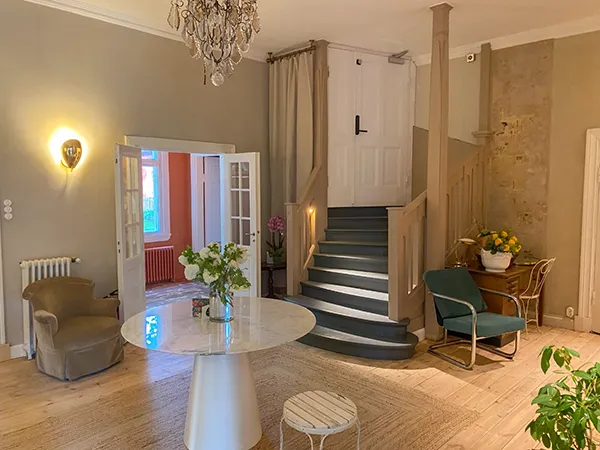 Elegant and cozy interior with a spacious open layout, featuring a round glass table, plush seating, and a decorative chandelier.